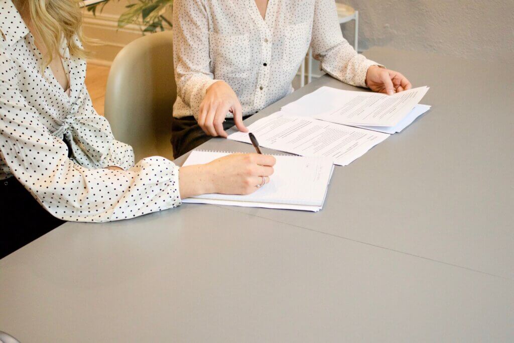 Two women sitting at a desk signing papers for a company loan.